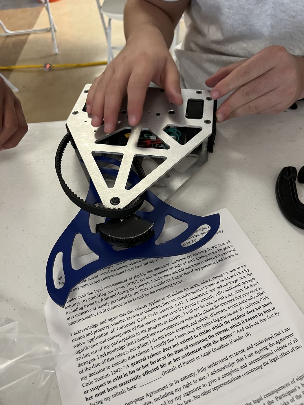 The robot mid-assembly at a competition table, belt drive to the weapon hub visible under the top plate.