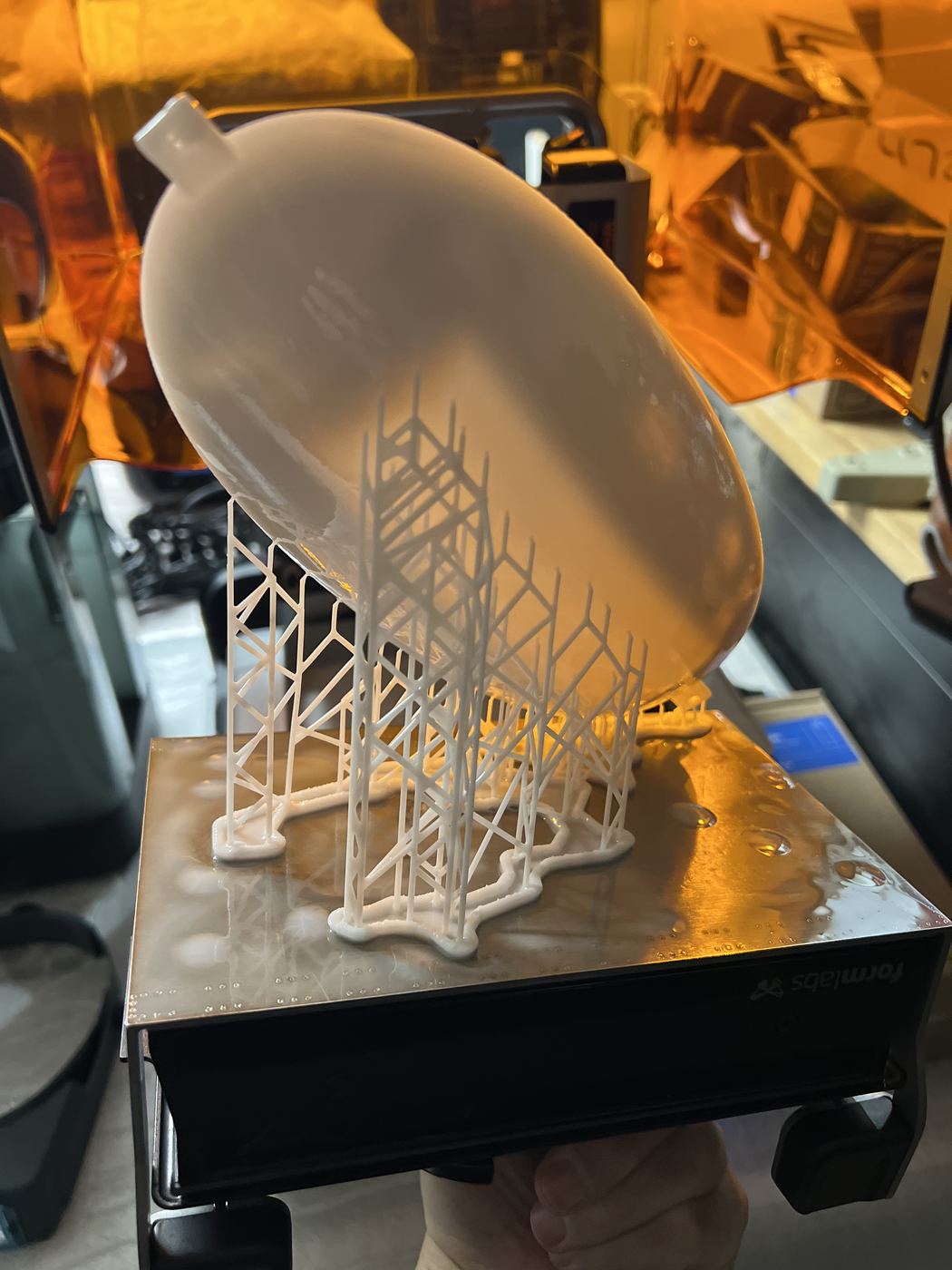 The capsule shell fresh off the printer, support lattice still attached to the build platform.